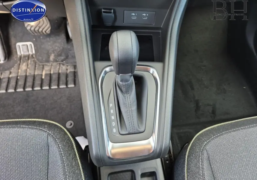 Vue plongeante sur la console centrale avec levier de vitesse automatique noir et sièges tissu gris à surpiqûres vertes.
