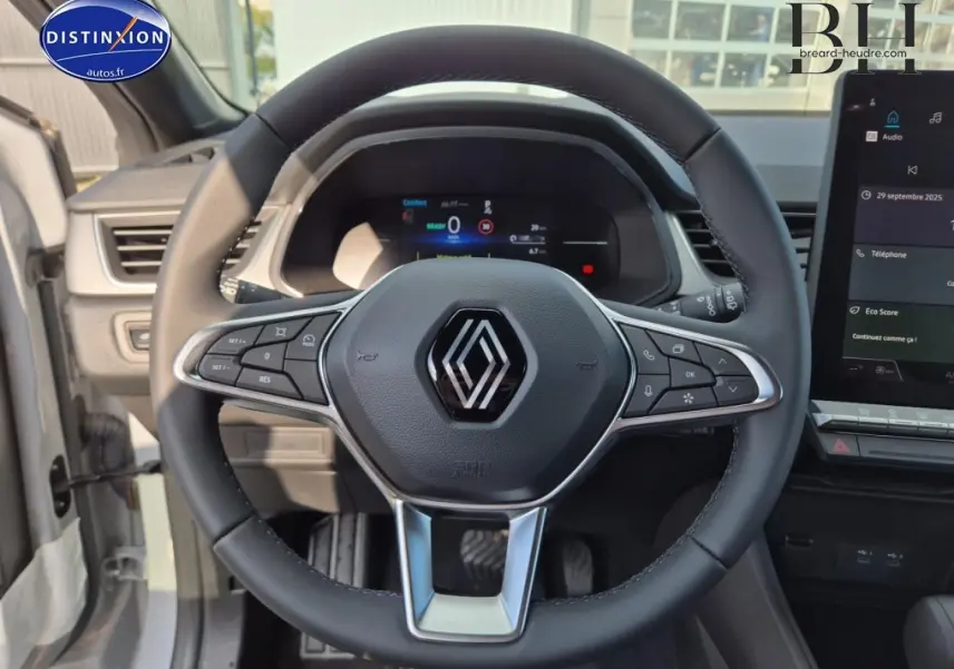 Vue rapprochée du volant multifonction noir avec logo Renault au centre, tableau de bord numérique et écran tactile à droite.