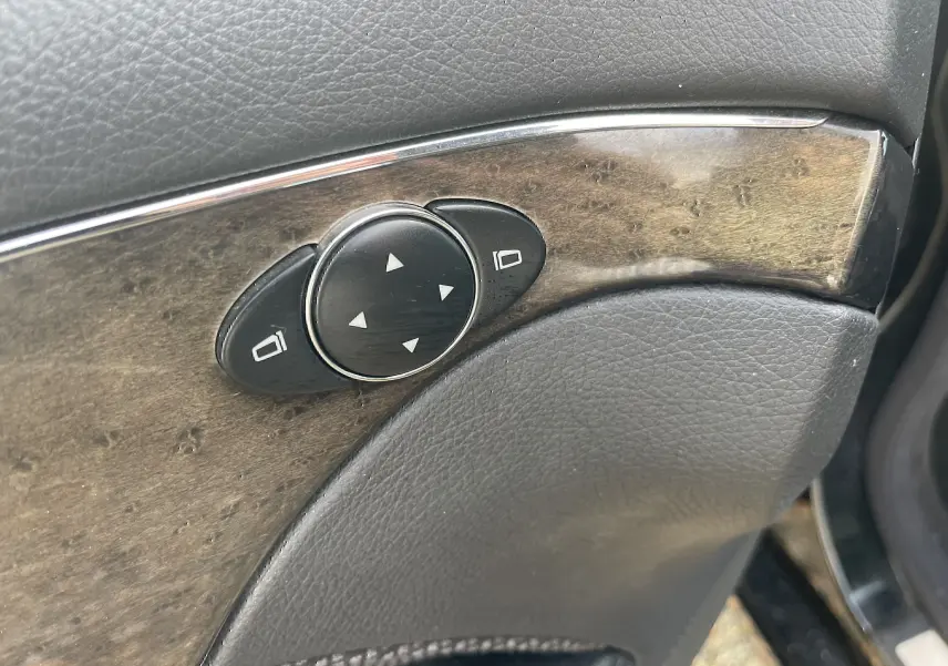 Détail du panneau de porte côté conducteur de la Mercedes Classe E 320 CDI noire de 2003, avec commandes de réglage des rétroviseurs.