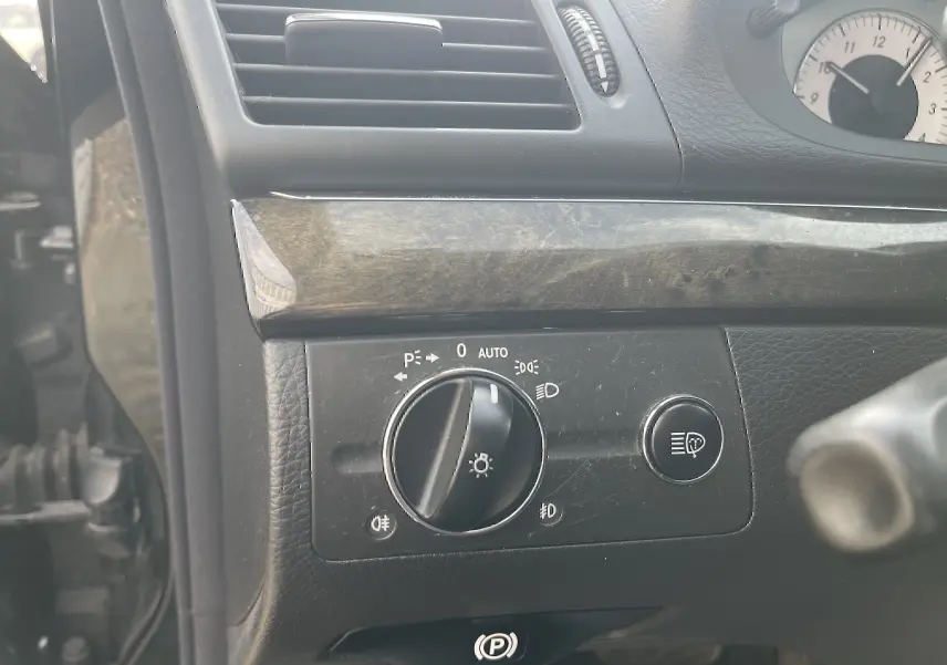 Détail du tableau de bord côté gauche d’une Mercedes Classe E 320 CDI noire de 2003, avec commande des phares et bouton de réglage.