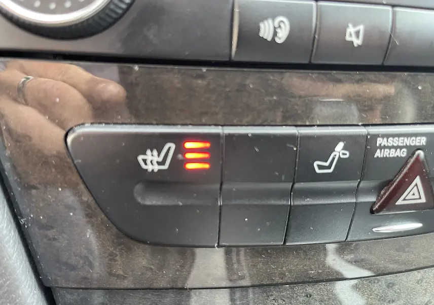 Détail du tableau de bord d’une Mercedes Classe E 320 CDI noire de 2003, bouton de siège chauffant activé avec trois voyants rouges.