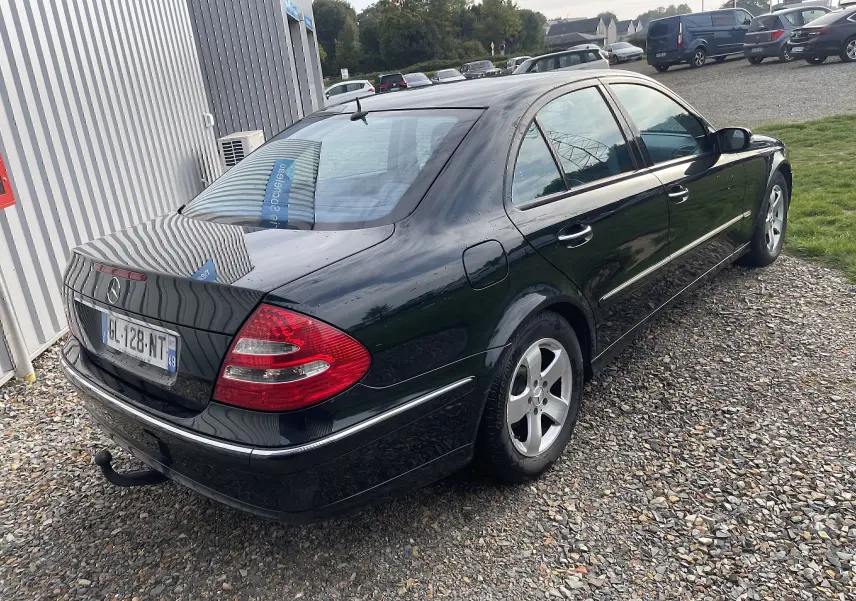 Vue 3/4 arrière droite d'une Mercedes Classe E 320 CDI Elegance noire de 2003 avec attelage et jantes alliage.