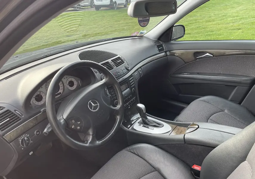 Intérieur de la Mercedes Classe E 320 CDI Elegance 2003, vue côté conducteur, tableau de bord noir avec inserts bois et boîte auto.