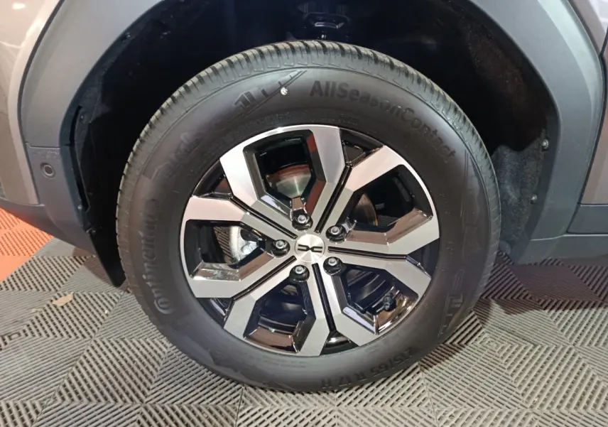 Gros plan sur la roue avant droite du Dacia Bigster gris foncé, mettant en valeur la jante noire et argentée au design moderne.