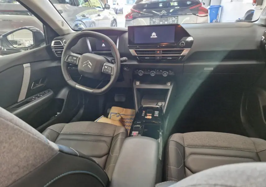 Vue intérieure avant de la Citroën C4 2024, avec tableau de bord noir et sièges en tissu gris et noir.