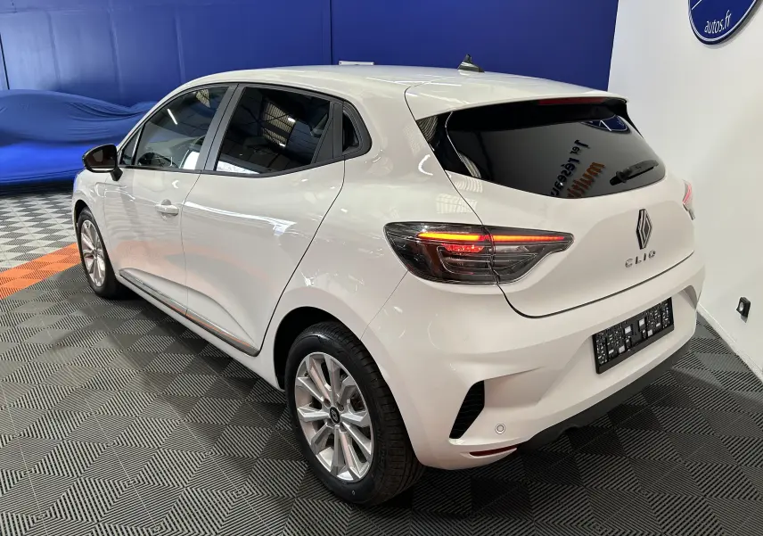 Renault Clio V blanche vue en 3/4 arrière droit, avec feux arrière allumés et jantes alliage 16 pouces.