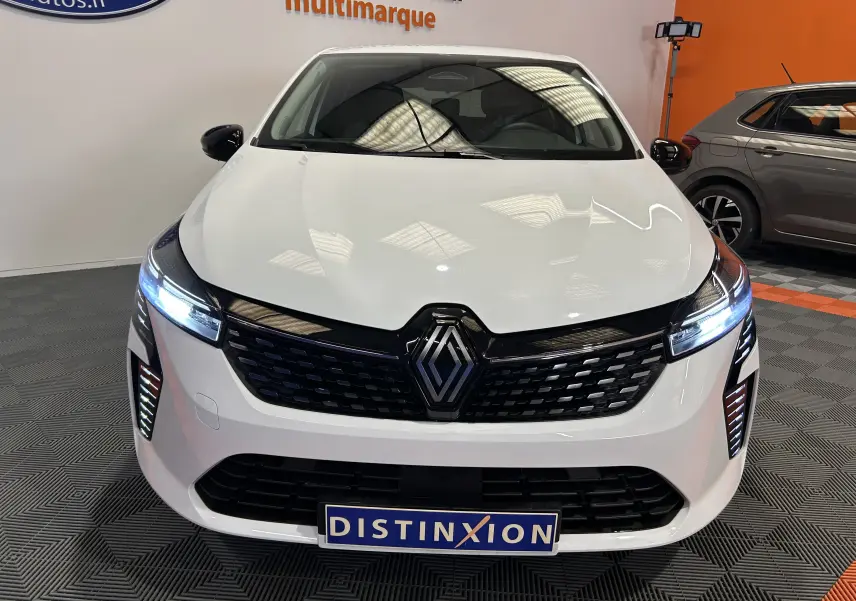 Vue avant d'une Renault Clio V blanche avec phares LED allumés et calandre noire dans un showroom.