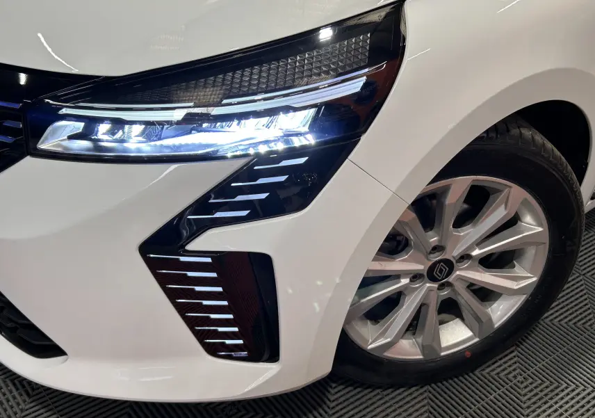 Gros plan sur l'avant droit blanc de la Renault Clio V 2025, mettant en valeur le phare LED et la jante alliage.