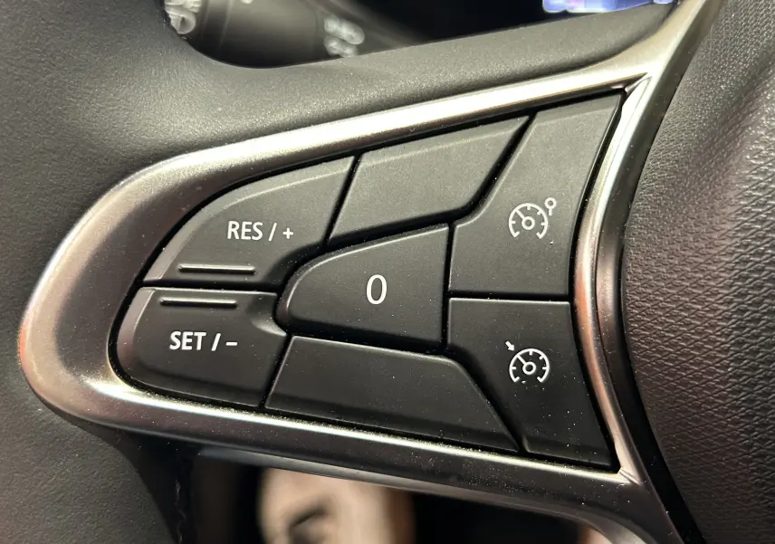 Gros plan sur les commandes de régulateur de vitesse au volant noir de la Renault Clio V TCE 90ch.