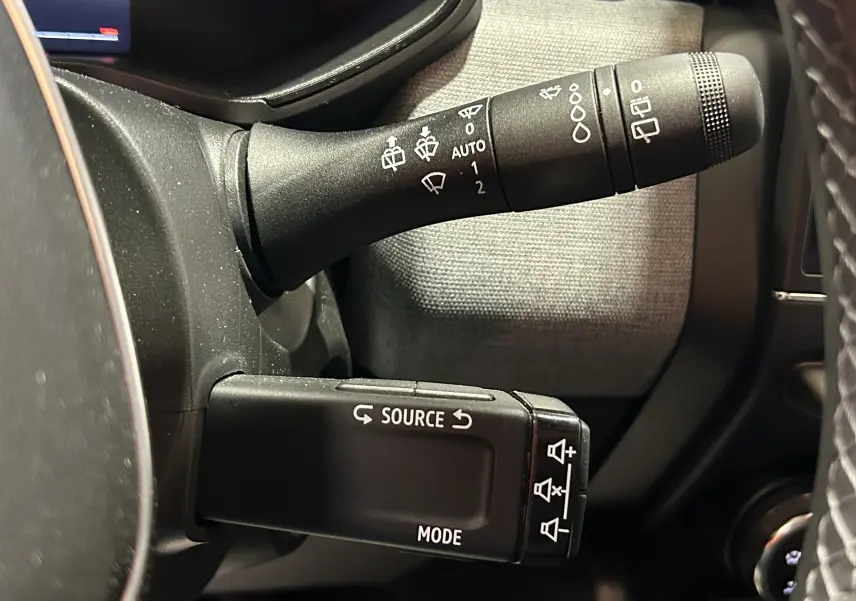 Gros plan sur les commandes au volant de la Renault Clio V blanche, avec les boutons source et mode bien visibles.