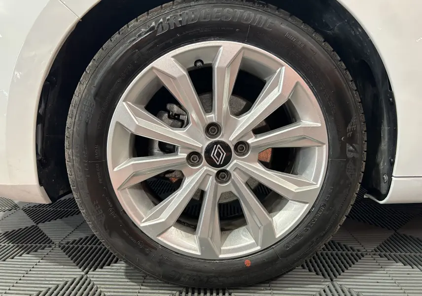 Gros plan sur la roue avant droite blanche d'une Renault Clio V avec jante alliage argentée et logo Renault central.