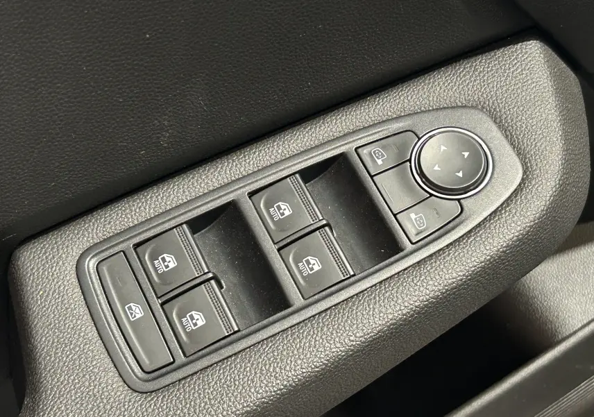 Gros plan sur les commandes de lève-vitres et réglage des rétroviseurs côté conducteur d'une Renault Clio V blanche.