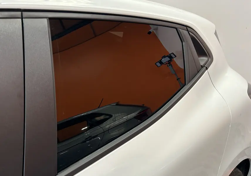 Gros plan sur la partie arrière droite blanche de la Renault Clio V, mettant en valeur la vitre latérale teintée et la poignée intégrée.