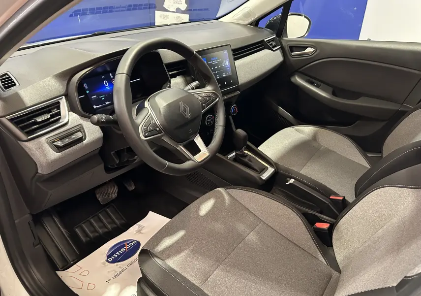 Vue intérieure côté conducteur de la Renault Clio V TCE 90CH avec tableau de bord numérique et sellerie tissu gris.