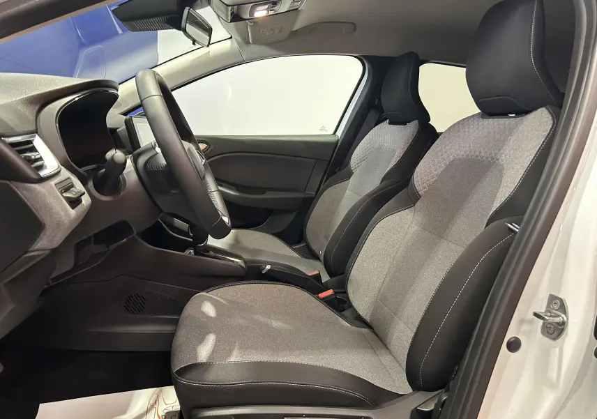 Vue intérieure côté conducteur de la Renault Clio V blanche 2025, sièges tissu gris et noir avec volant multifonction.