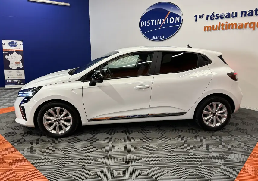 Profil côté gauche de la Renault Clio V blanche 5 portes, avec jantes alliage et vitres teintées, en intérieur showroom.