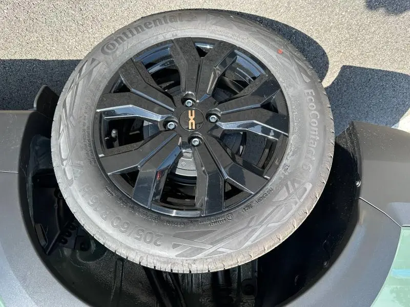 Gros plan sur la roue de secours noire avec jante alu noire du Dacia Jogger blanc, visible dans le coffre ouvert.