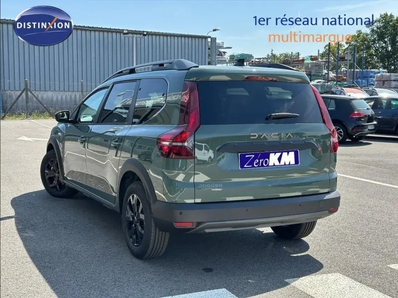 Vue 3/4 arrière droite d'un Dacia Jogger vert avec barres de toit et vitres arrière surteintées.