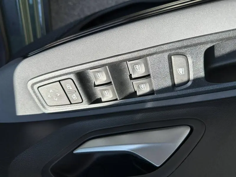 Gros plan sur les commandes de lève-vitres et rétroviseurs côté conducteur du Dacia Jogger blanc, avec poignée de porte argentée.