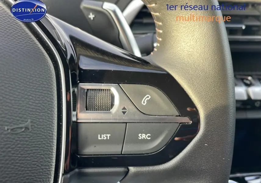 Gros plan sur les commandes audio au volant cuir noir du Peugeot 3008 hybride 2024, côté gauche.