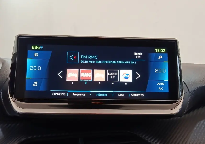 Écran tactile central affichant la radio FM sur Peugeot 208 Electrique Roadtrip, intérieur avec finition carbone.