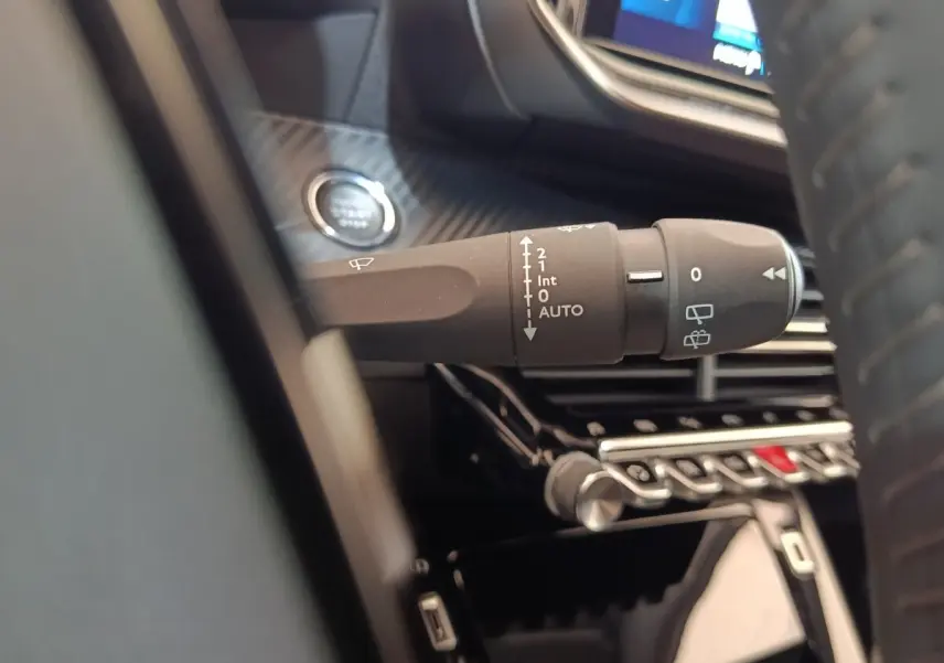 Gros plan sur la commande d’essuie-glace à gauche du volant dans l’habitacle noir d’une Peugeot 208 Electrique gris clair.