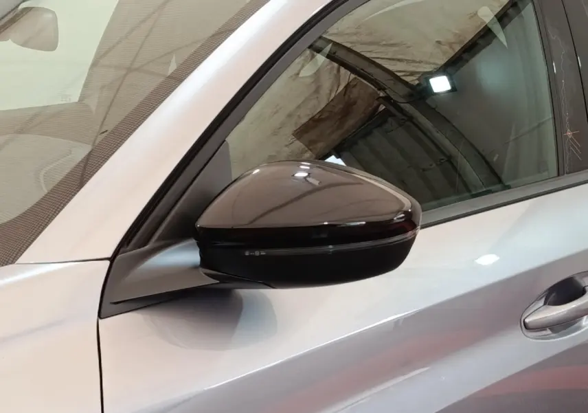 Rétroviseur côté gauche noir brillant sur Peugeot 208 électrique gris clair, vue rapprochée en intérieur.