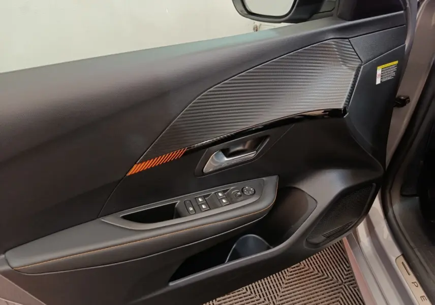 Vue rapprochée de la porte avant gauche gris clair de la Peugeot 208 Electrique ROADTRIP avec insert décoratif noir et orange.