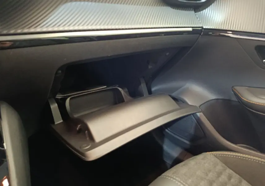 Vue intérieure côté passager du Peugeot 208 électrique gris clair, avec boîte à gants ouverte et détails de sellerie visible.