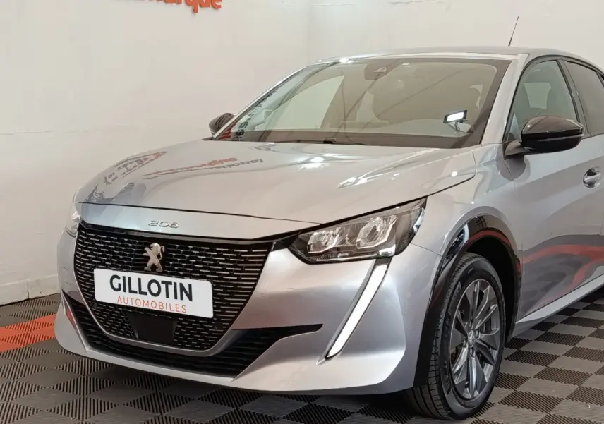 Vue 3/4 avant droit d'une Peugeot 208 électrique gris clair avec calandre noire et feux LED verticaux.