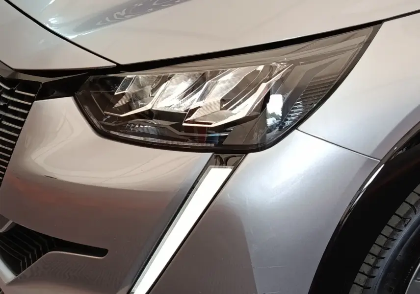 Gros plan sur le phare avant droit LED et la carrosserie gris clair d'une Peugeot 208 Electrique ROADTRIP 2022.