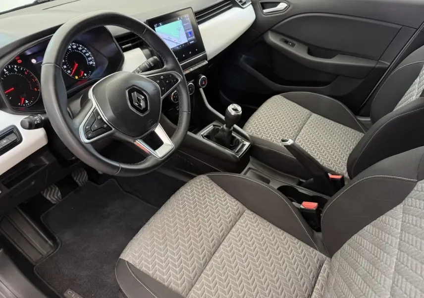 Vue intérieure côté conducteur de la Renault Clio 2023 avec volant cuir, écran tactile central et sièges gris à motifs.
