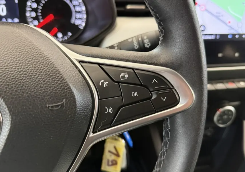 Gros plan sur le volant cuir synthétique noir de la Renault Clio 2023 avec commandes multifonctions et tableau de bord partiel.