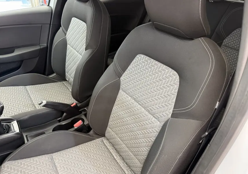 Vue intérieure côté conducteur de la Renault Clio blanche 2023, sièges tissu gris à motifs géométriques et coutures blanches.