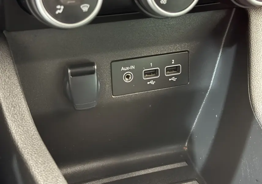Gros plan sur la console centrale noire de la Renault Clio blanche Evolution TCe 100 GPL, montrant les ports USB et Aux-IN.