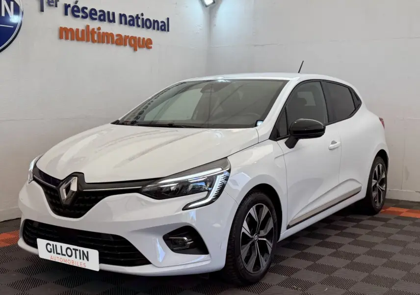 Renault Clio blanc vue 3/4 avant droit, avec phares LED et jantes alliage noires, en intérieur showroom.