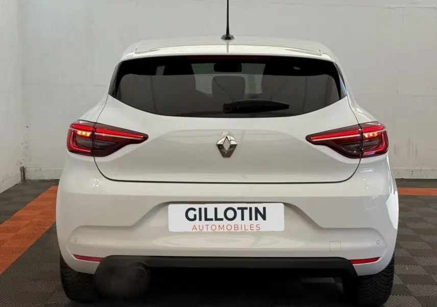 Vue arrière d'une Renault Clio blanche Evolution TCe 100 GPL avec feux arrière allumés dans un garage.