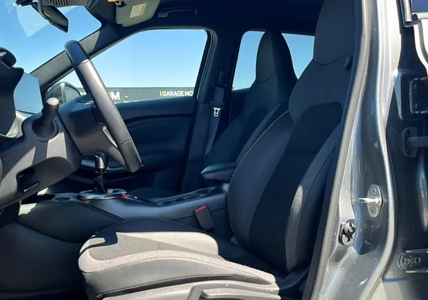 Vue intérieure côté conducteur du Nissan Juke gris 2025, avec sièges mixtes noir et gris et volant cuir multifonction.