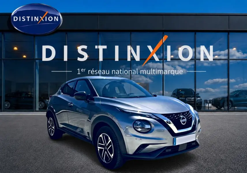 Nissan Juke gris 3/4 avant droit, avec jantes alu et calandre distinctive, devant une vitrine Distinxion.