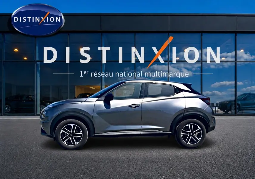 Profil droit d'un Nissan Juke gris 2025 garé devant une vitrine avec jantes alliage et toit noir contrasté.