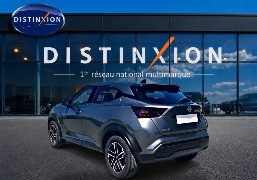 Vue 3/4 arrière droite d'un Nissan Juke gris 2025 avec jantes alu et feux arrière LED, devant une vitrine Distinxion.