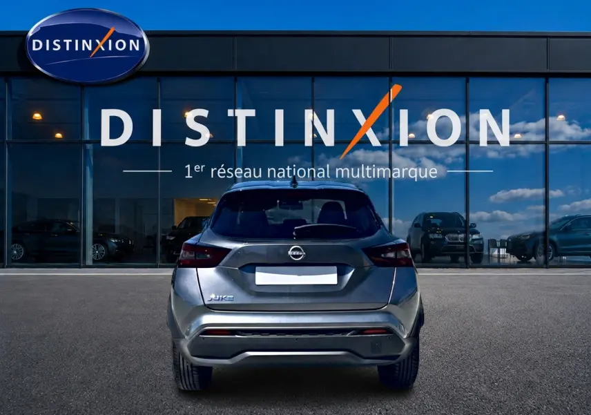 Vue arrière d'un Nissan Juke gris 2025 garé devant une vitrine avec logo Distinxion visible.