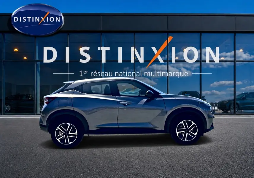 Nissan Juke gris en profil droit devant une vitrine avec logo Distinxion, jantes alliage et lignes dynamiques.