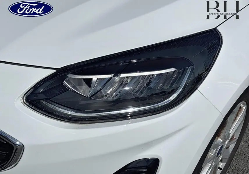 Gros plan sur le phare avant droit et la jante alu d'une Ford Fiesta blanche Glacier 2023, finition Titanium Business.