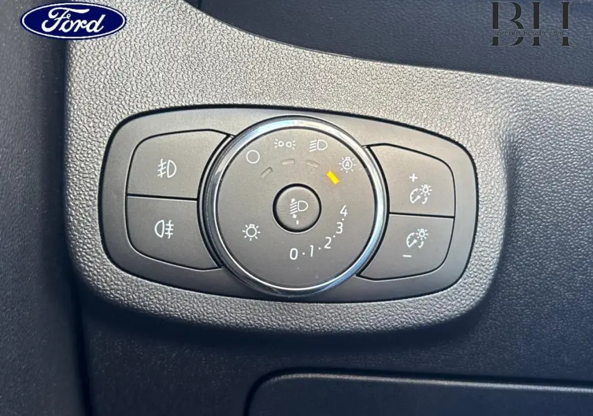 Gros plan sur le bouton de réglage des phares dans l’habitacle noir de la Ford Fiesta Blanc Glacier 2023.