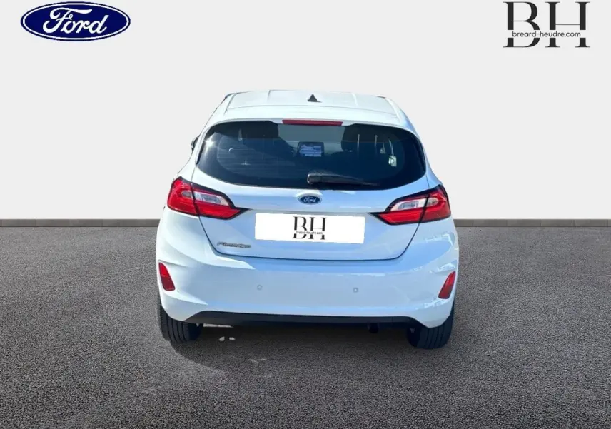 Vue arrière d'une Ford Fiesta blanc glacier 2023 avec feux LED et becquet arrière, sur sol goudronné.
