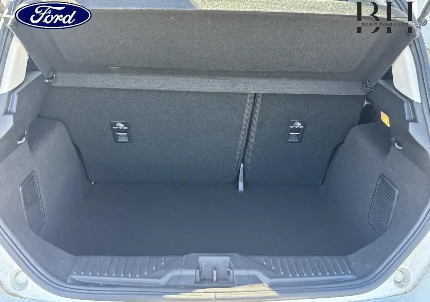 Coffre ouvert vu de l'arrière d'une Ford Fiesta 2023 blanc Glacier, montrant l'espace de rangement vide et la banquette rabattable.
