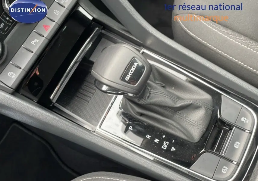 Vue rapprochée de la console centrale avec levier de vitesse automatique noir marqué SKODA, sièges tissu gris visibles.