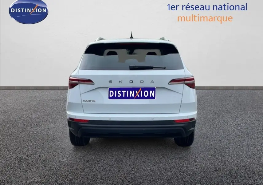 Vue arrière d'un Skoda Karoq blanc glacier 2025 avec vitres arrière surteintées et logo distinctif au centre.