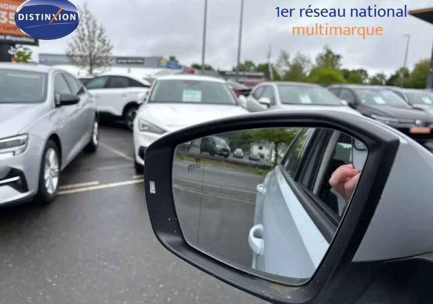 Rétroviseur côté droit d'un Volkswagen T-Roc blanc argent, avec reflet de la portière et main visible.